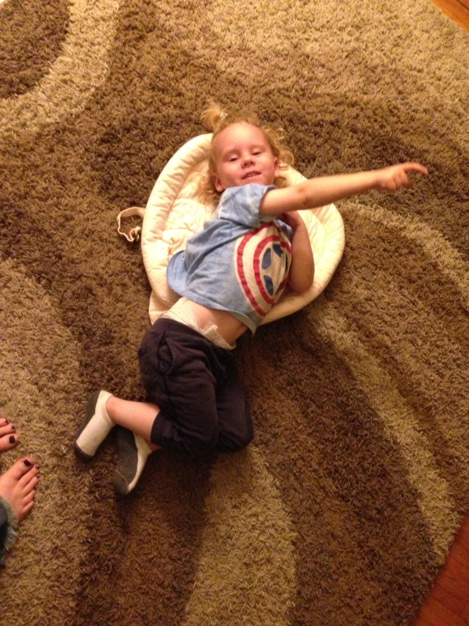 Giant toddler, pointing at his baby picture, attempting to fit into his Ergo infant insert.